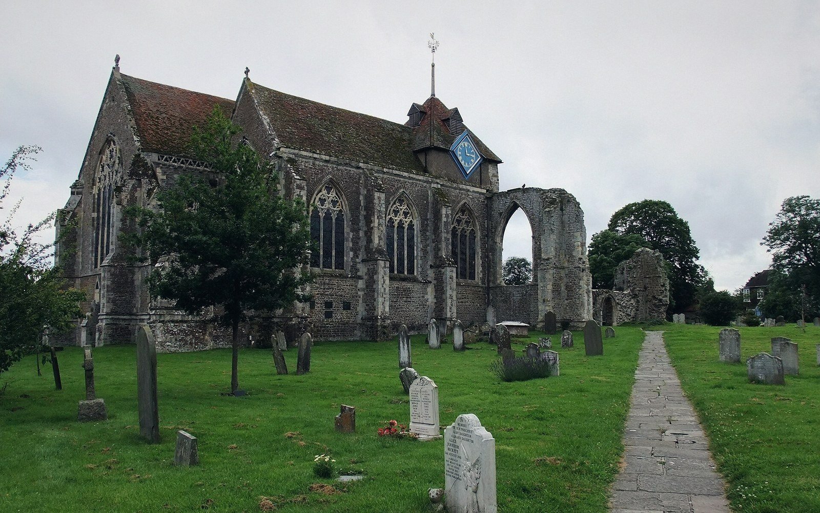 Stone church with clock tower stands amid a grassy graveyard filled with headstones