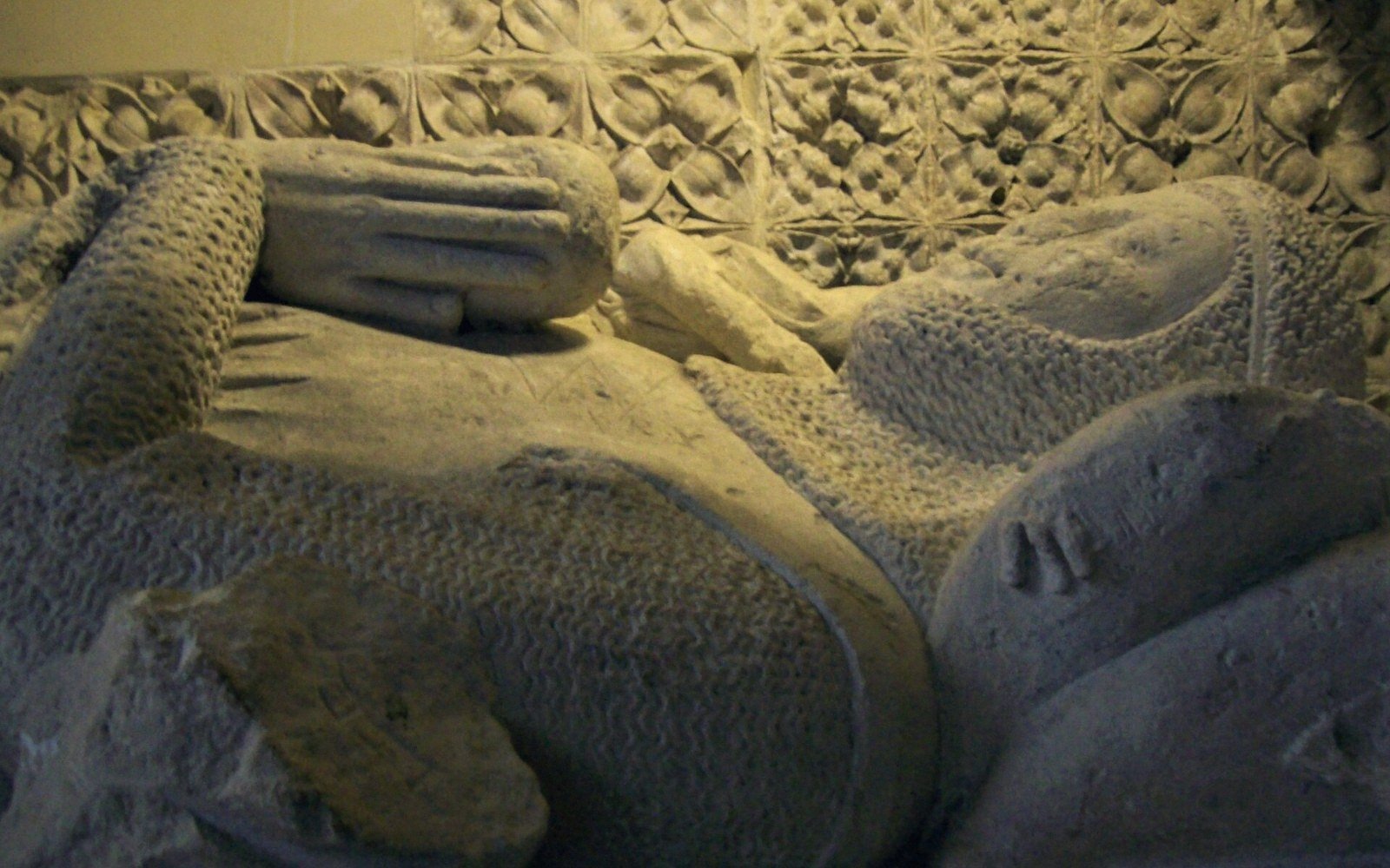 Stone effigy in chainmail armour lies on a carved medieval tomb