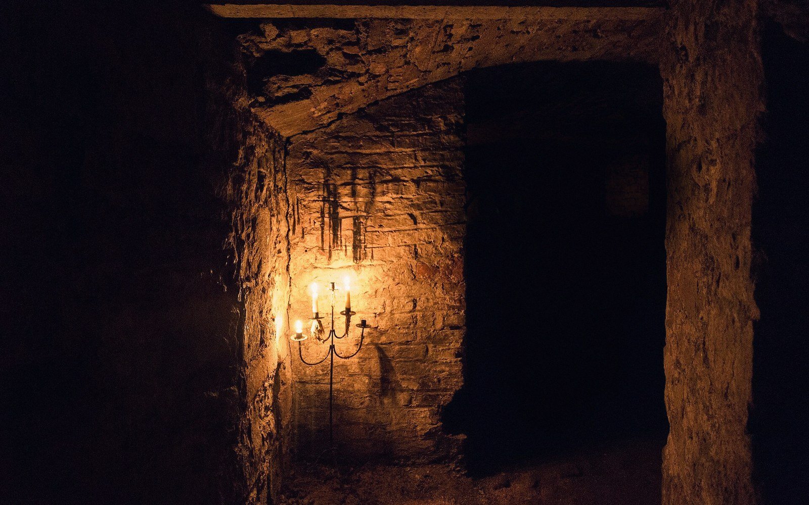 A lit candelabra glows against stone walls in a dark vaulted cellar