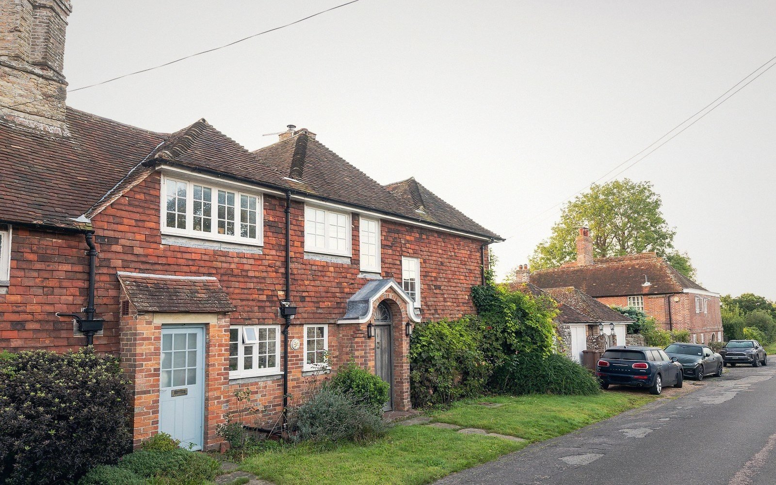 Brick cottages with tiled roofs line a quiet village street with parked cars